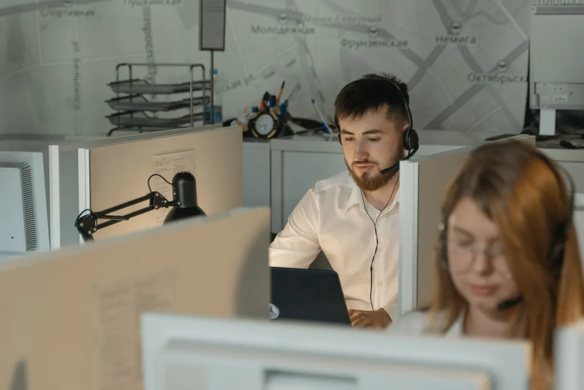 Un agent du service client avec un casque répond à des messages à son bureau, en lien avec les habitudes de reporting qui maintiennent les métriques de service sous contrôle.