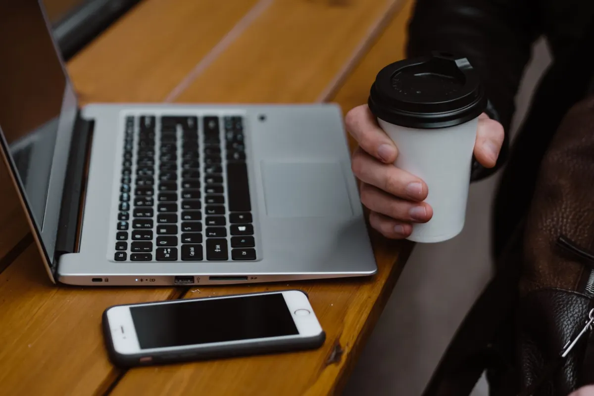 Quelqu'un consulte son téléphone à son bureau avec un café le matin, un instant lié au bon timing pour publier aux heures de forte activité.