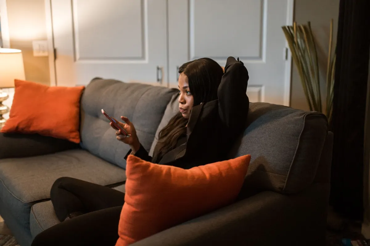 Eine Frau entspannt sich abends auf dem Sofa und scrollt auf ihrem Handy, wenn das Instagram-Engagement tendenziell seinen Höhepunkt erreicht.