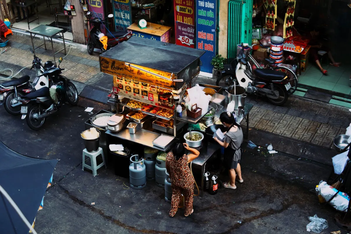 Un vendedor de comida callejera atiende una sartén chisporroteante en un mercado al aire libre, la clase de escena que combina con hashtags de viajes culinarios como #streetfoodlover.