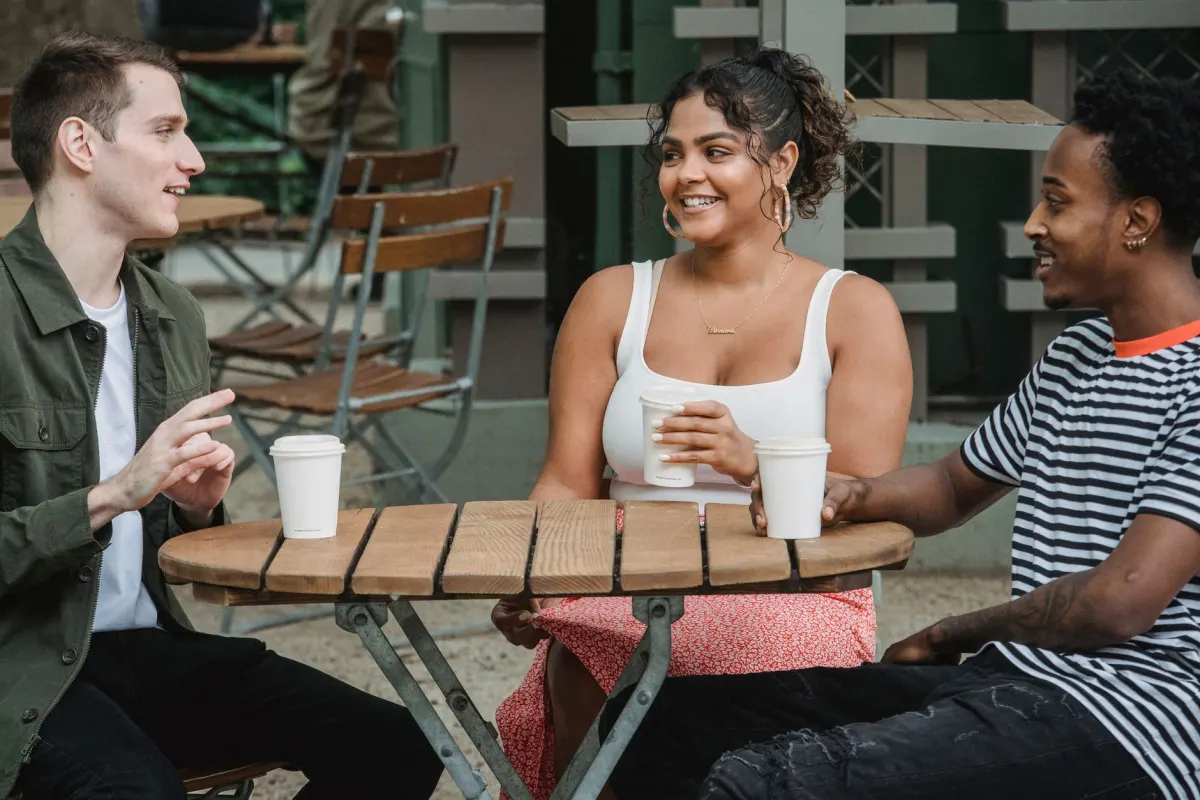 Un pequeño grupo de amigos conversando frente a un café en una mesa compartida, el tipo de vínculo cara a cara que la construcción de comunidad intenta crear en línea.