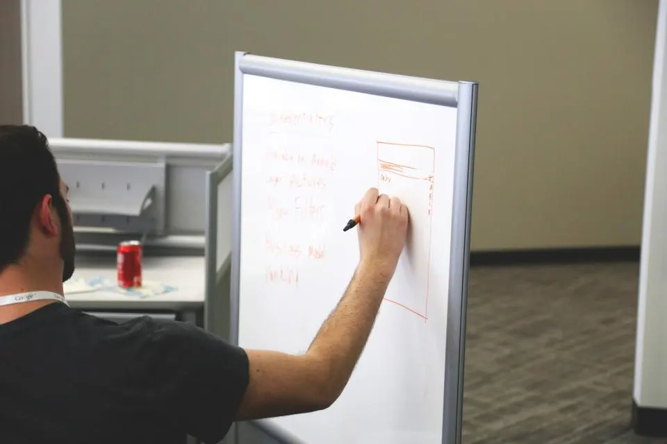 Jemand listet Differenzierungsmerkmale an einem Whiteboard auf und skizziert daneben ein Layout, ein schneller Weg zum Entwurf einer ersten Positionierungskarte.