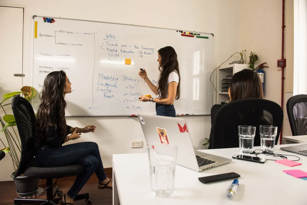 Uma equipe de marketing discute a estratégia de canais em um quadro branco, ilustrando por que o marketing digital é importante.