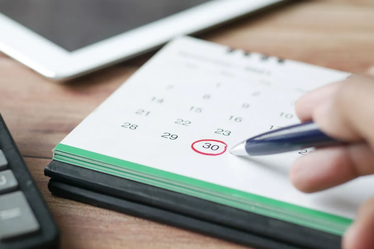 Una mano tachando una fecha en un calendario de pared de papel, para ilustrar el cambio o la cancelación de un post programado.
