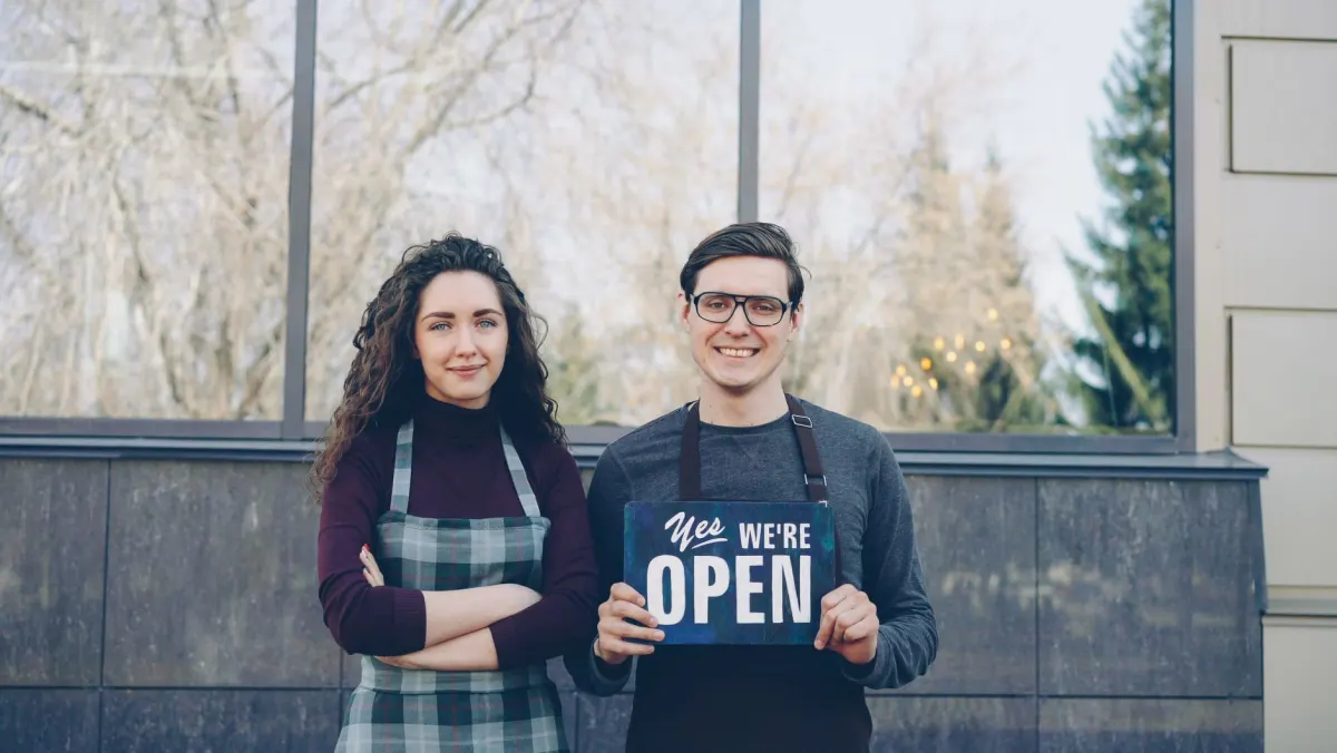 Une propriétaire de petite entreprise sourit devant sa boutique, le genre de moment personnel qui fonctionne bien partagé dans un statut.