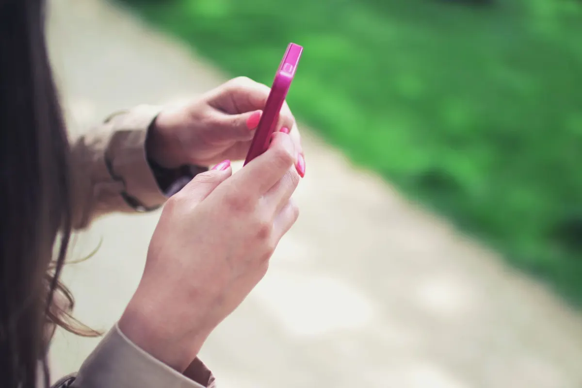 Mãos digitando uma resposta em um smartphone, o tipo de mensagem pessoal que uma pessoa real escreve, não um bot.