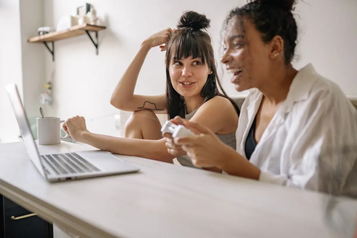 Freunde lachen zusammen über Laptops während eines Spieleabends, der Art von wiederkehrendem Event, das Community-Gewohnheiten aufbaut.