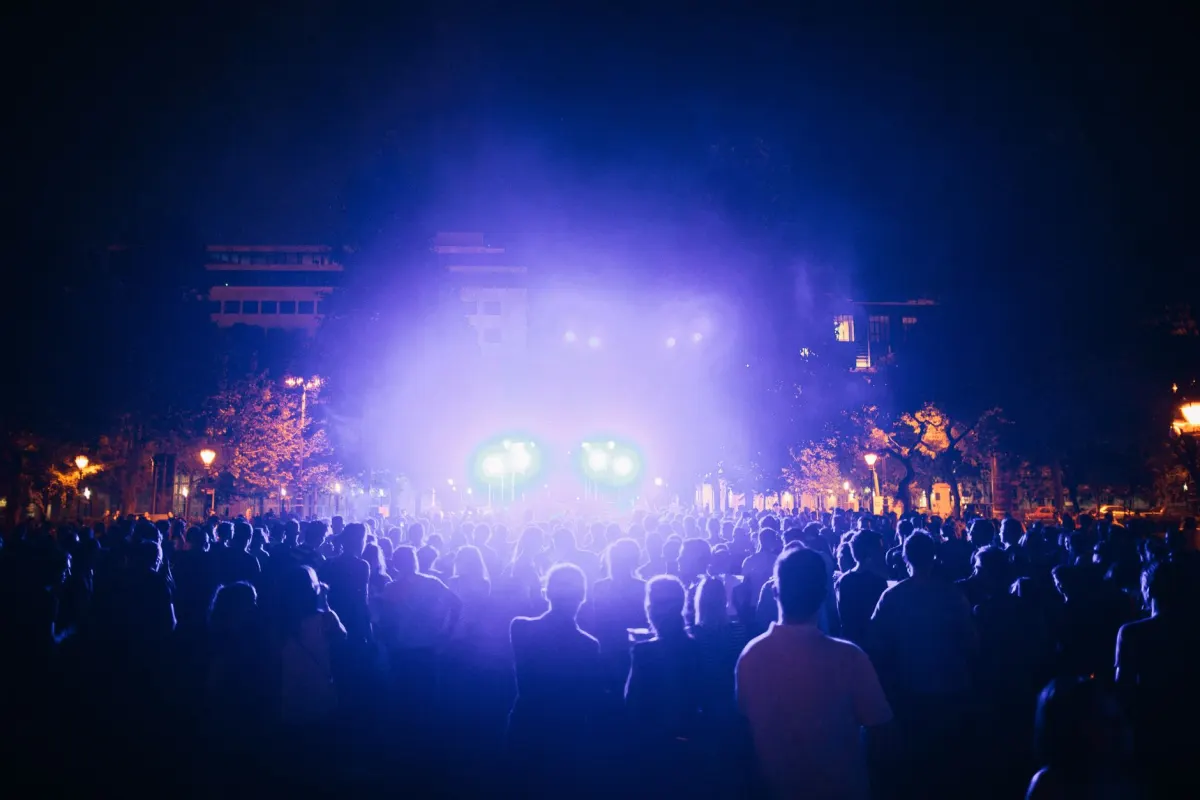 Uma multidão em um show levanta celulares sob luzes roxas do palco, um momento fã associado ao coração roxo.