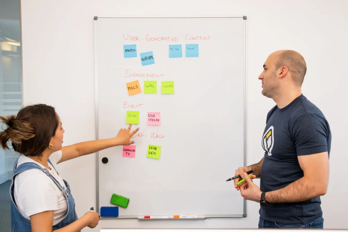 Zwei Kollegen vergleichen Notizen an einem Whiteboard, neben dem Abschnitt, der die Funktionen gegenüberstellt.