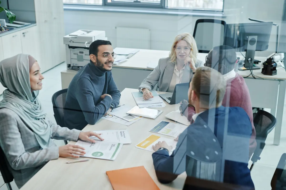Ein kleines Team versammelt sich in einem Büro um einen Tisch, passend zur Diskussion über Agenturen mit vielen Kundenkonten.