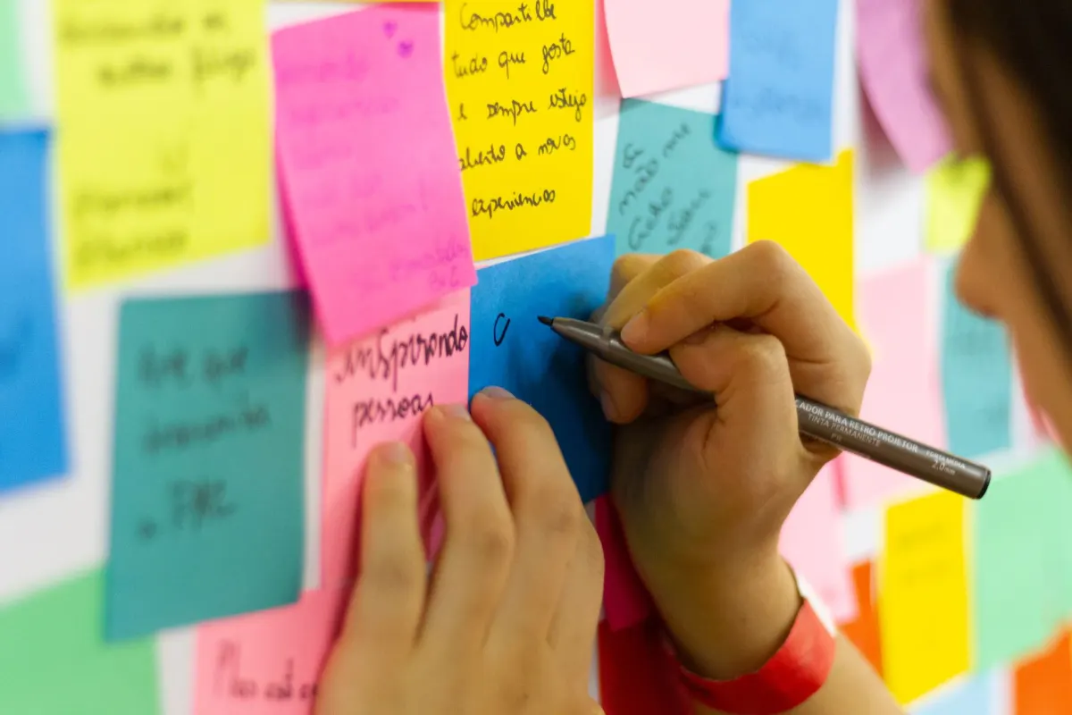 Uma pessoa anota ideias em post-its em uma mesa, ilustrando a busca por novas ideias de conteúdo.