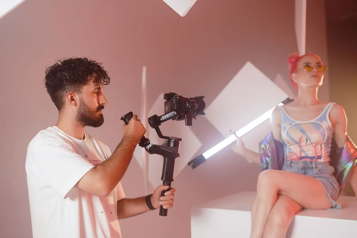 Um fotógrafo grava vídeo vertical num pequeno estúdio, refletindo uma sessão de produção de vídeo em lote.