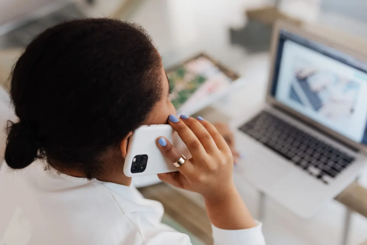 A marketer glances between a phone and a laptop at a cluttered desk, the kind of app-switching that eats a workday.