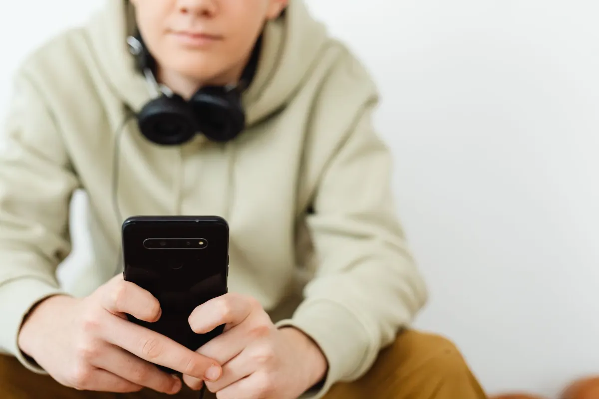 Um adolescente olha para um celular no quarto, remetendo às configurações de segurança da conta discutidas nesta seção.