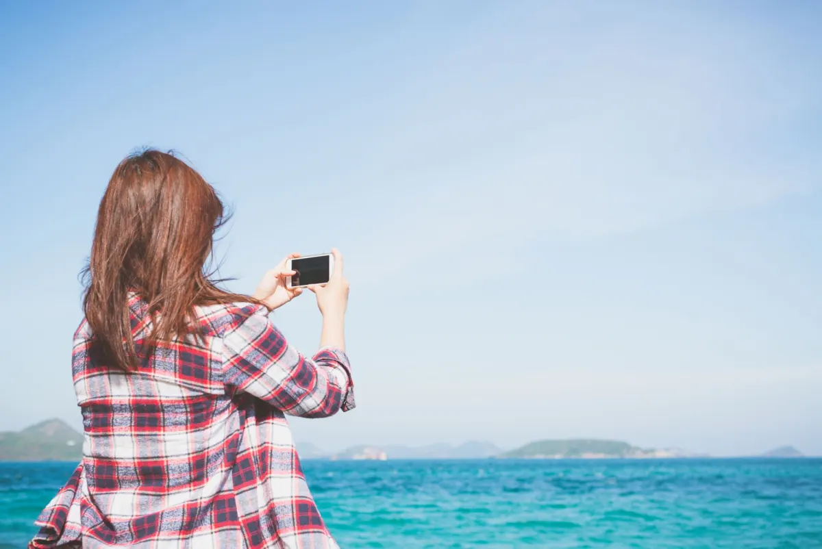Une femme consulte son téléphone avant d'ajouter une localisation à une publication, illustrant les tags de localisation.