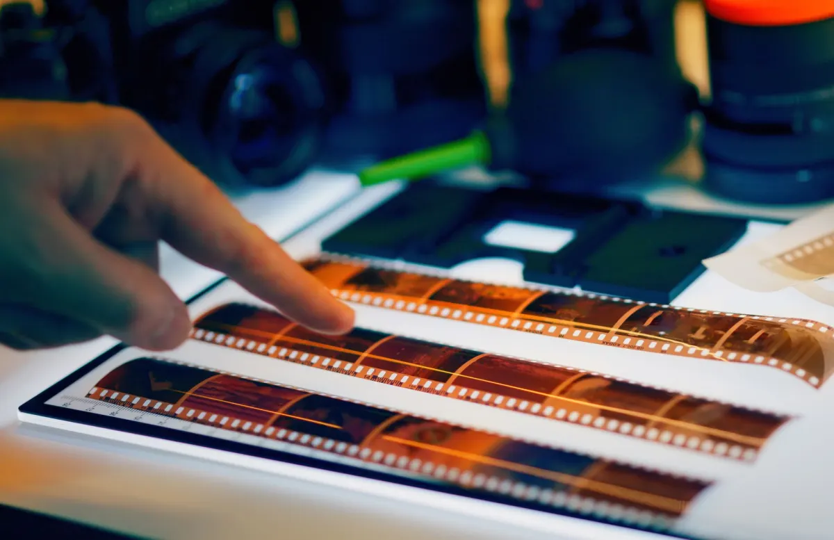 A photographer holds a strip of film negatives over a lightbox, the kind of scanned source that once carried the retired softwareImage code.