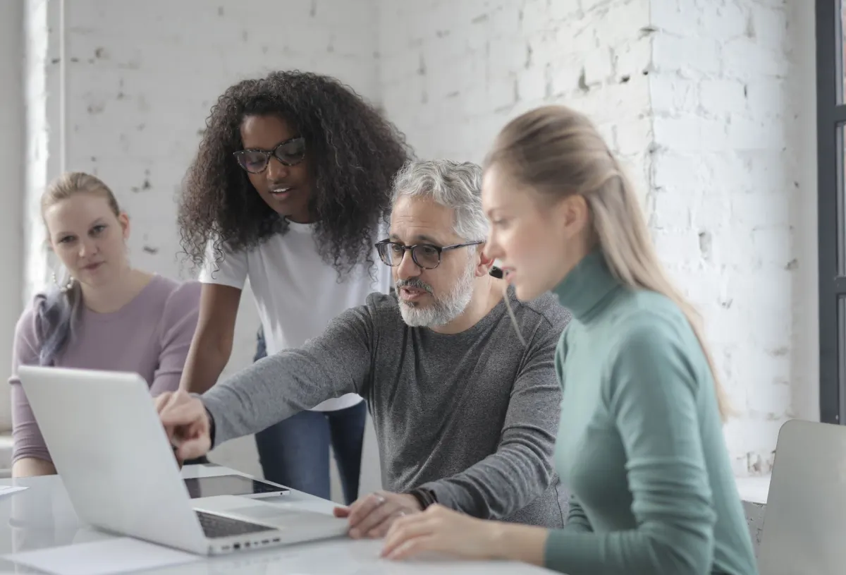Un pequeño equipo se reúne alrededor de una laptop en una reunión, reflejando el enfoque en colaboración en equipo de herramientas como Planable.
