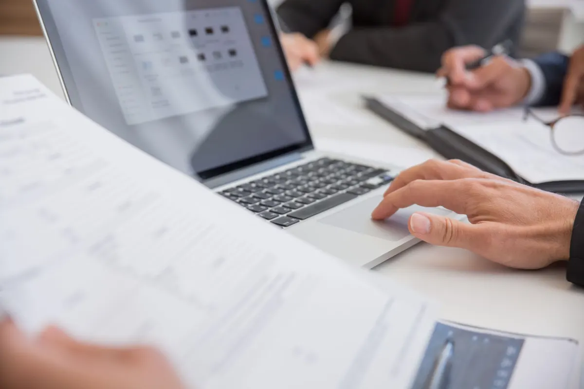 A professional reading a draft on a laptop at a desk before approving it, the review step a Contributor key enforces.