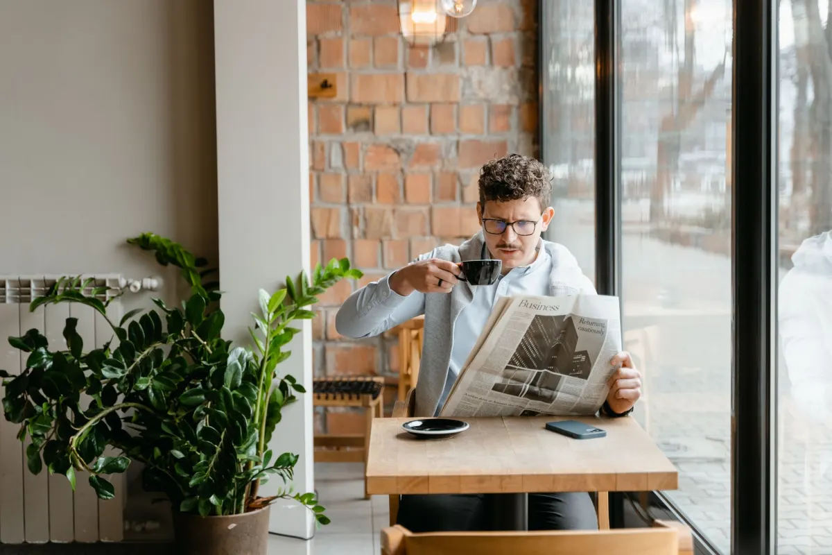 Eine Person liest an einem Tisch eine Zeitung, stellvertretend für die Print- und Onlinequellen, die Marken verfolgen.