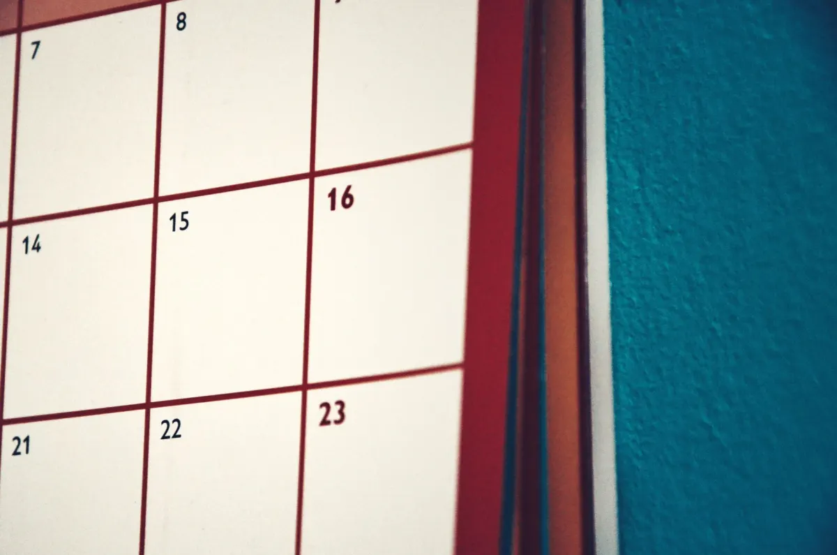 Una mano marca fechas en un calendario de pared, como imagen de planificar un mes de publicaciones programadas de una sola vez.