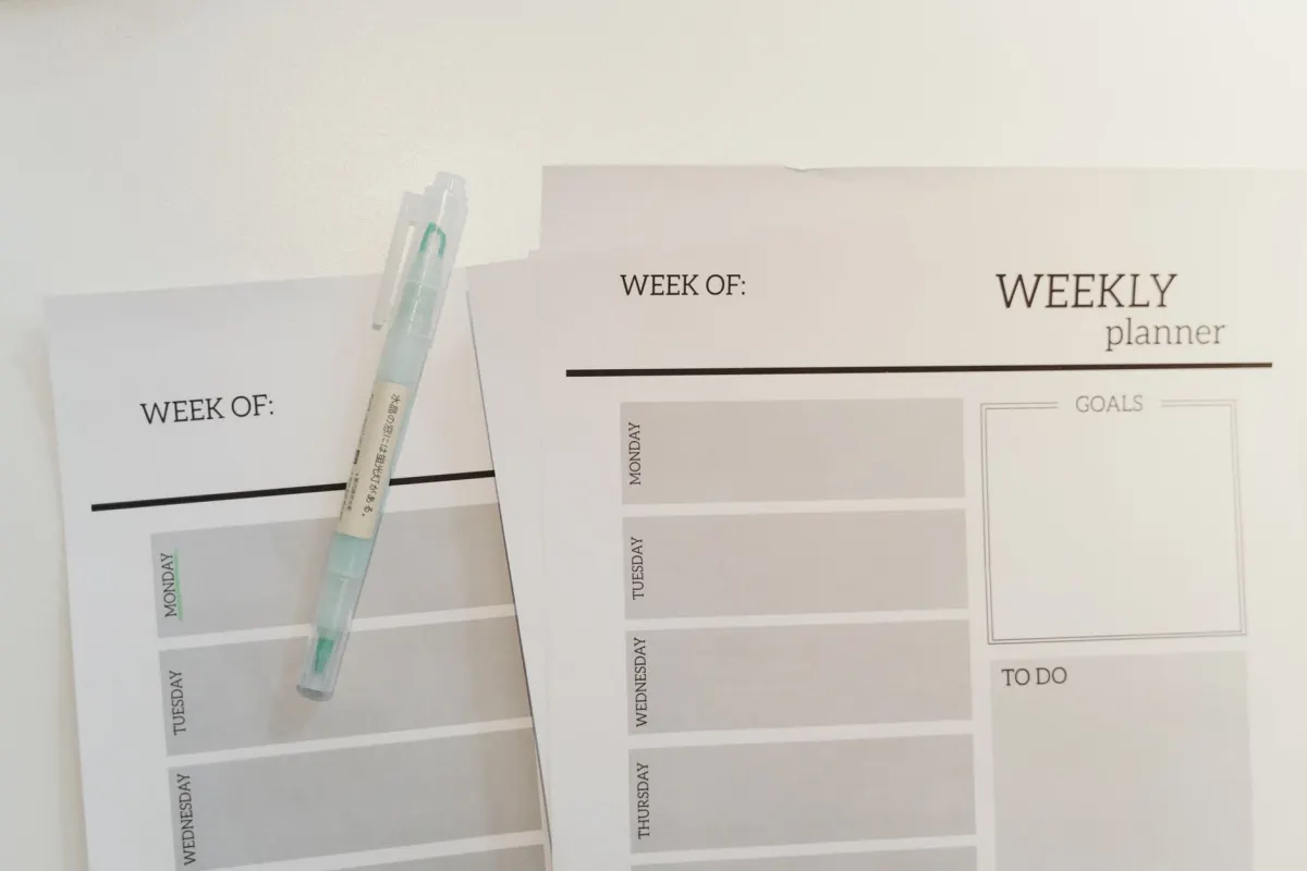 A hand fills in a paper weekly planner on a desk, standing for the posting cadence a dot keeps running through recurring tasks.