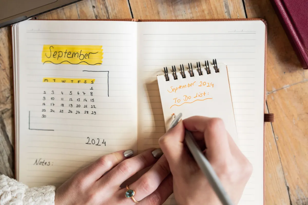 Eine Person skizziert von Hand einen woechentlichen Content-Kalender in einem Notizbuch.