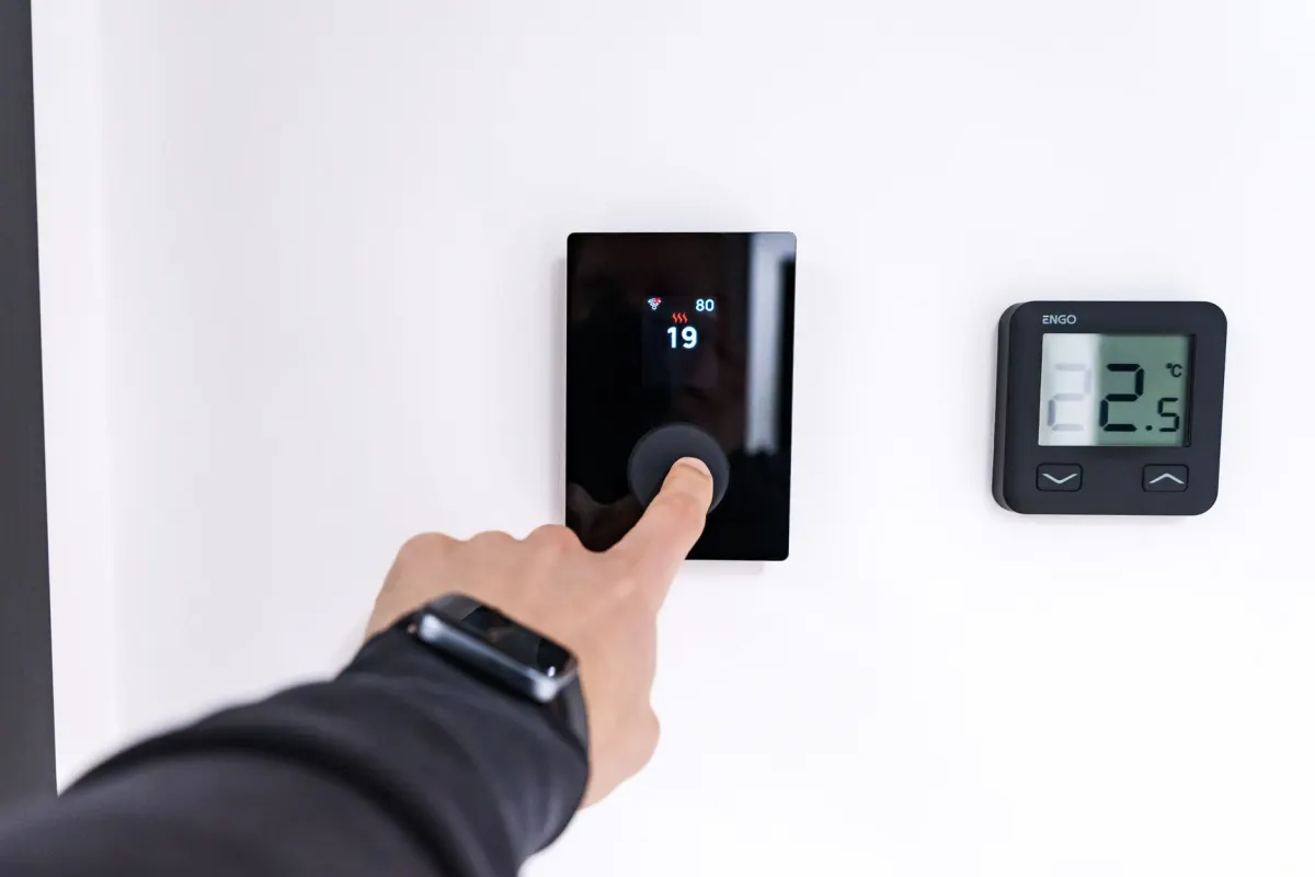 Una mano ajusta un termostato inteligente en la pared, el tipo de dispositivo que Home Assistant conecta y automatiza.