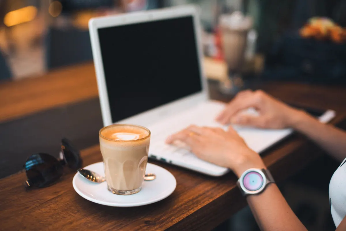 Eine Frau tippt an einem Cafétisch auf einem Laptop, ein Sinnbild für die Stunden, die Social-Media-Manager wöchentlich mit dem Schreiben von Bildunterschriften verbringen.