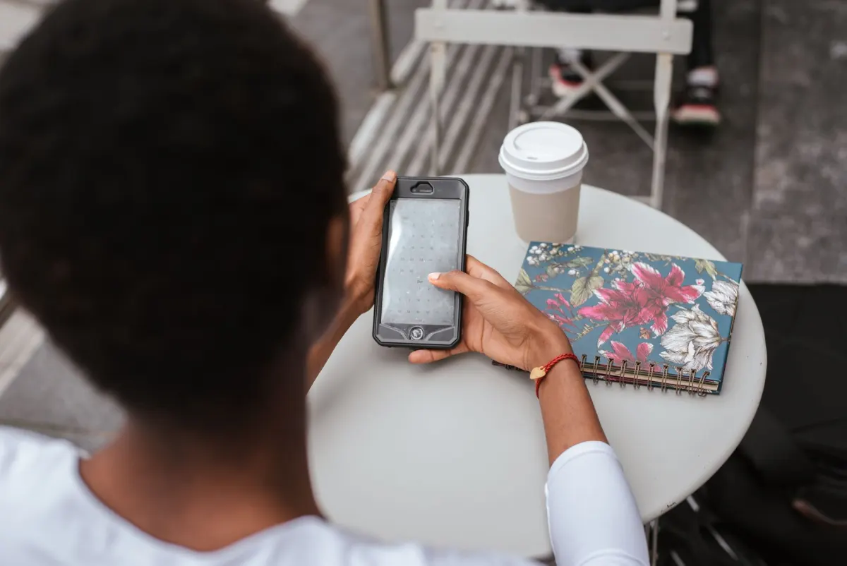 Eine Frau tippt eine Caption auf ihrem Handy in einem Cafe, der Moment, in dem eine erste Zeile entsteht.