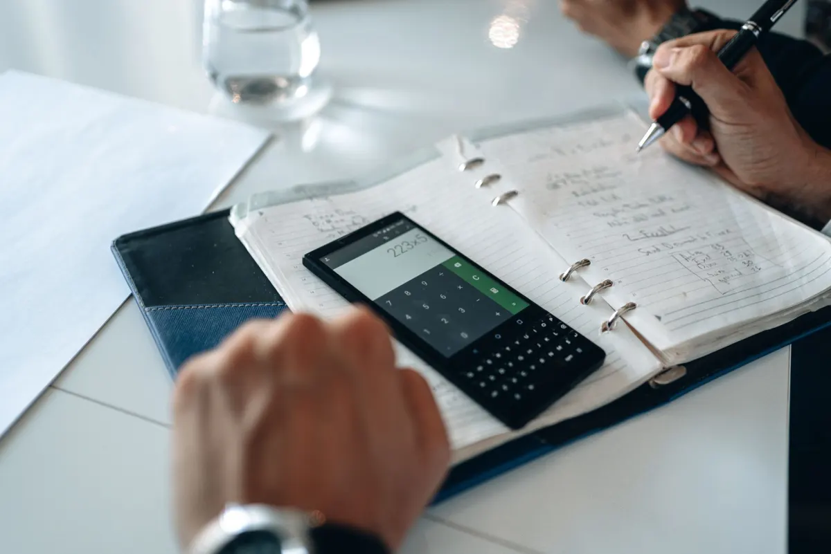 Eine Person nutzt eine Taschenrechner-App auf dem Smartphone an einem Schreibtisch, passend zu den plattformspezifischen Formeln in diesem Abschnitt.