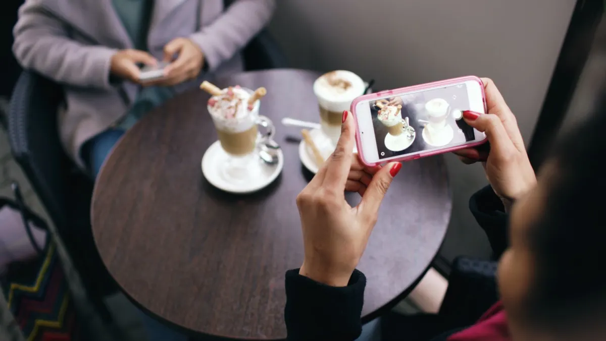 Ein Barista fotografiert einen fertigen Latte mit dem Handy, bevor der Morgenansturm beginnt.