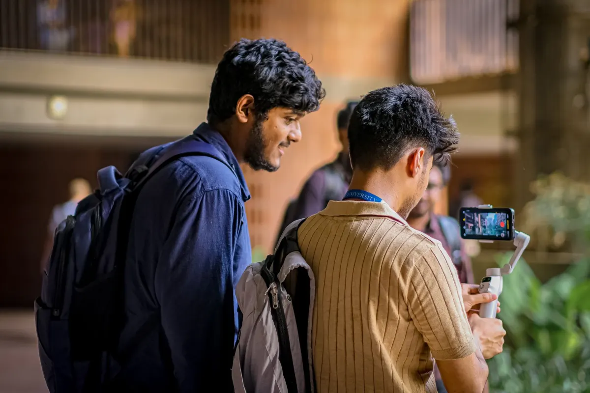 A student sets up a phone on a tripod outside a dorm to film content for the university's social channels.