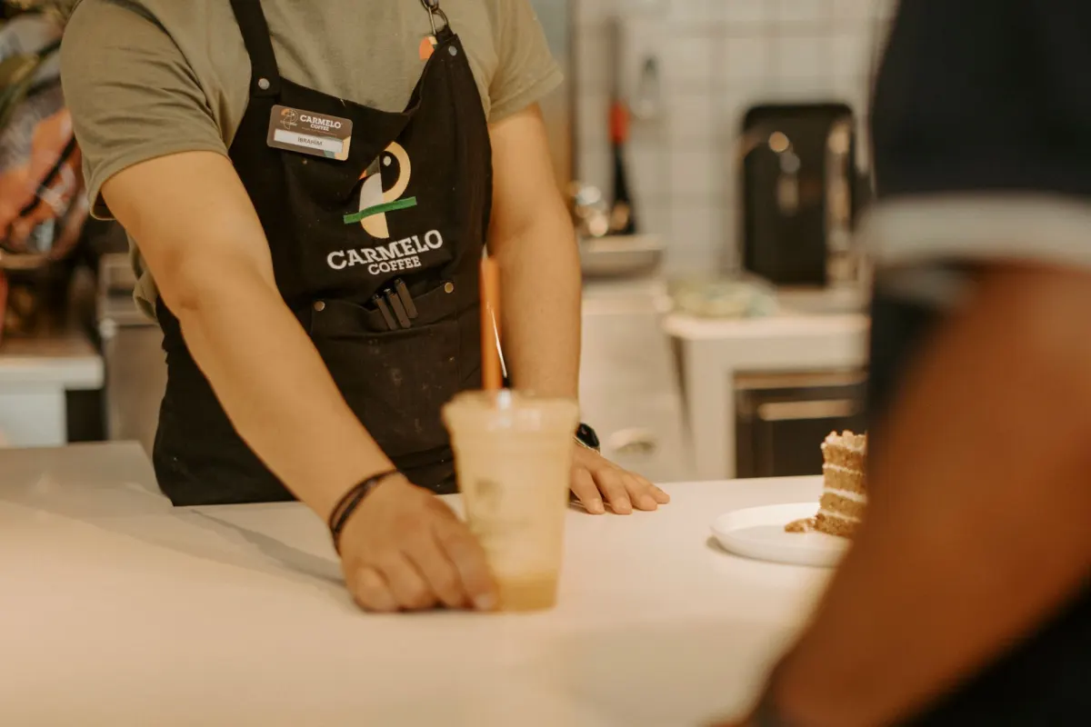 Ein Barista reicht einer Kundin ueber die Theke einen Becher, der Alltagsmoment, den ein Nachbarschafts-Business zu Social-Content macht.