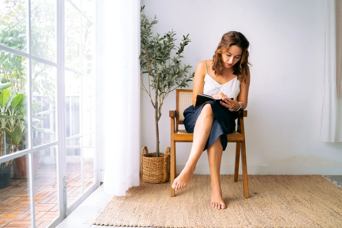 Une personne écrit dans un journal entourée de plantes d'intérieur, reflétant les loisirs personnels mis en avant dans ce style de bio.