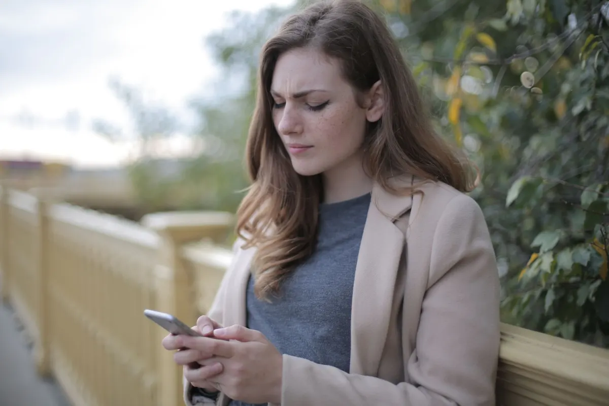 Una mujer mira su teléfono con el ceño fruncido, mostrando la confusión de intentar averiguar si una publicación vaga habla de ella.