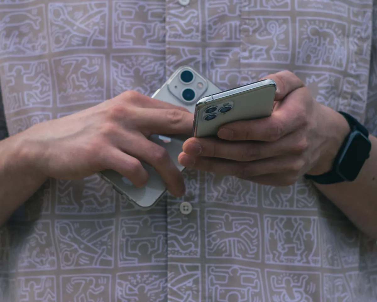 Eine Person hält zwei Smartphones gleichzeitig, was den doppelten Arbeitsablauf beim Jonglieren getrennter Planungstools zeigt.