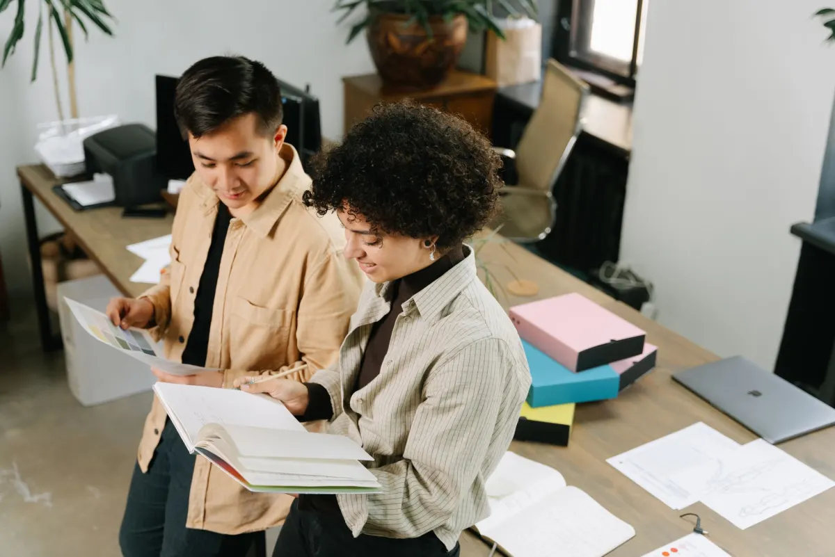 Deux collègues examinent des dépliants marketing imprimés sur un bureau, une scène qui illustre la coordination nécessaire pour garder le contenu des partenaires conforme à la marque.