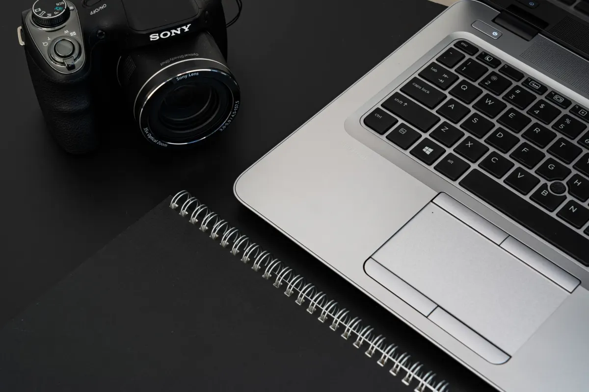 Uma mesa com laptop, câmera e caderno lado a lado, ligada à seção seguinte sobre a bio portfólio.