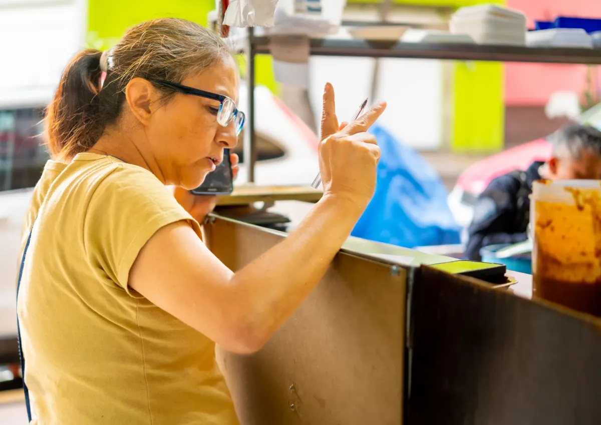 Una mujer usa un smartphone antiguo en un mercado al aire libre, el tipo de dispositivo y conexión para el que se creó TikTok Lite.