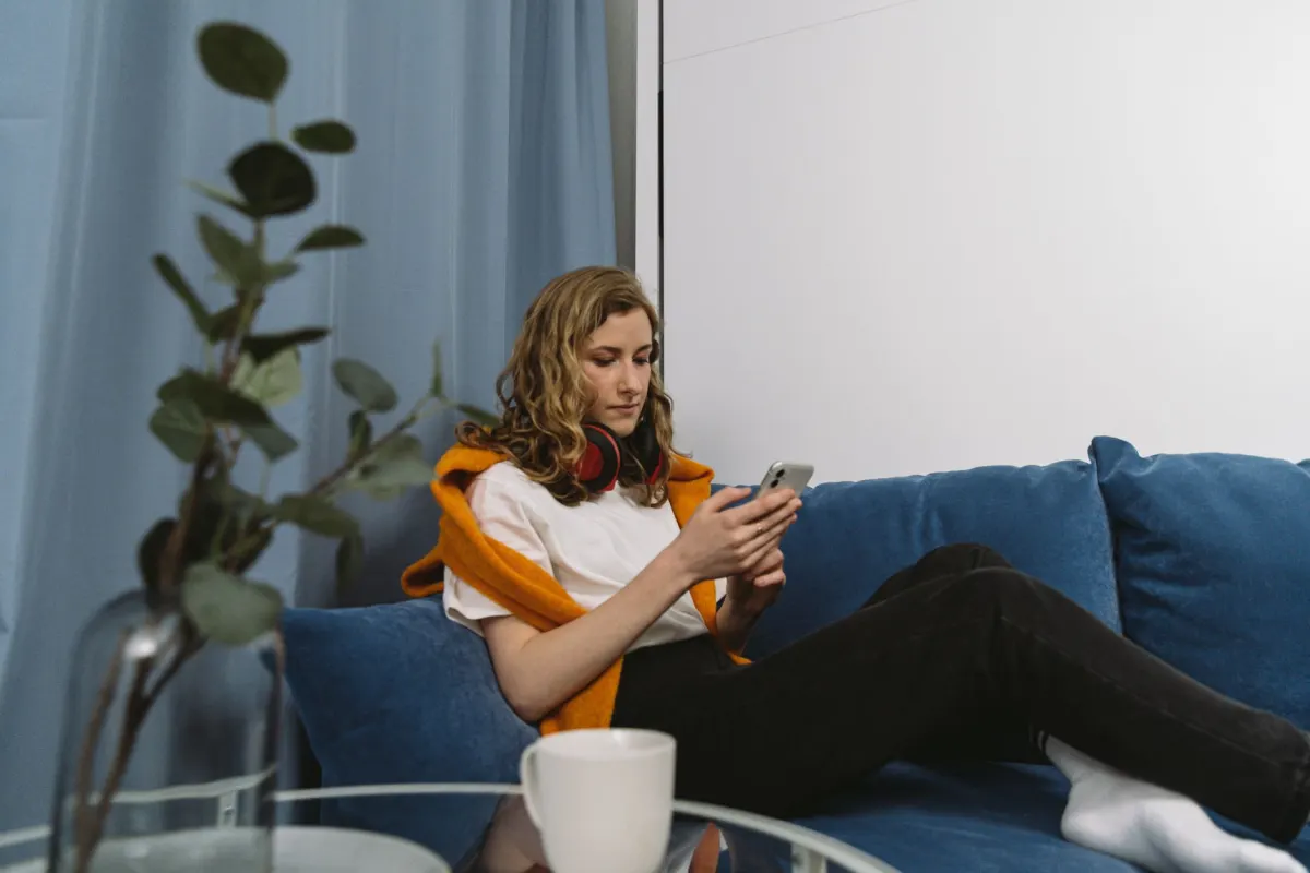 Eine Person scrollt auf dem Sofa am Handy, genau das Verhalten, auf das eine algorithmische Timeline ausgelegt ist.