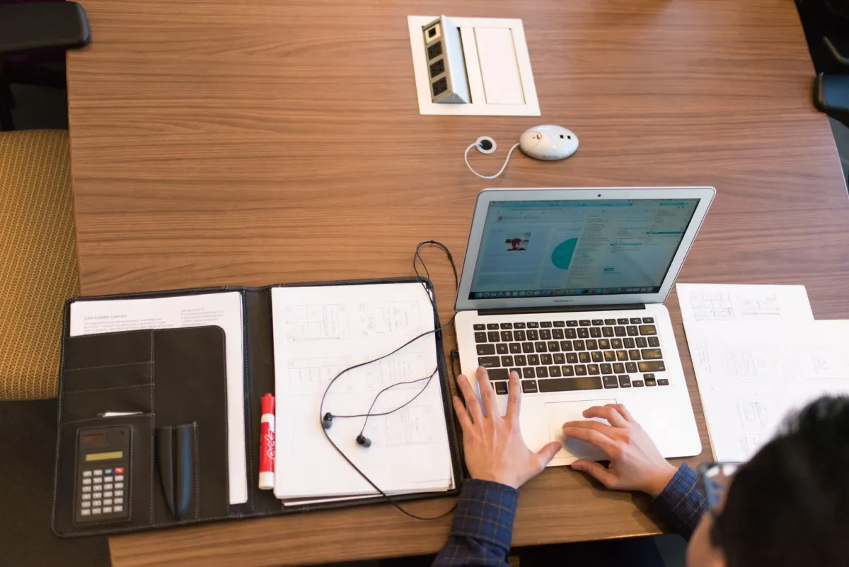 Una persona escribe en un portátil junto a una agenda de papel, reflejando el trabajo de programación que implica publicar en los momentos óptimos.