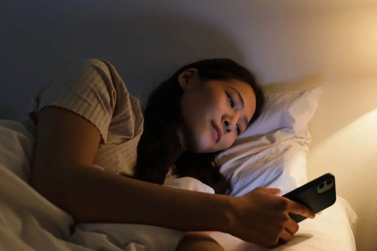 Una mujer está en la cama revisando su teléfono de noche, en sintonía con la pregunta discreta que suele transmitir un mensaje TTM.