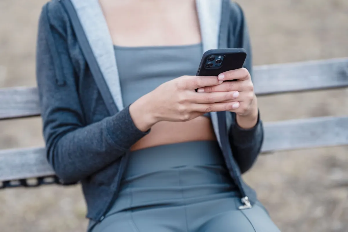 Una persona está sentada afuera desplazándose por su teléfono, un reflejo del uso cotidiano de redes sociales donde TTM aparece en distintas plataformas.