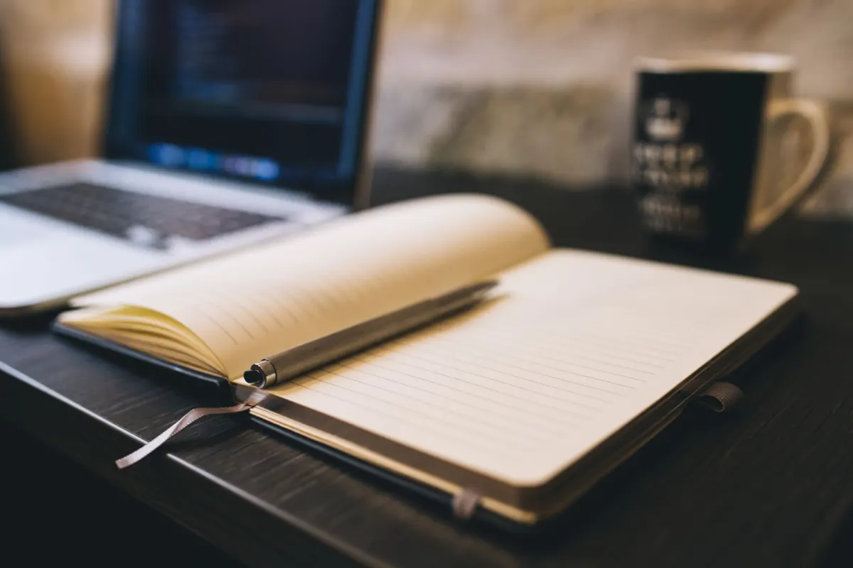 Un ordinateur portable ouvert à côté d'un carnet sur un bureau, évoquant le processus de rédaction et de relecture d'une publication avant sa mise en ligne.