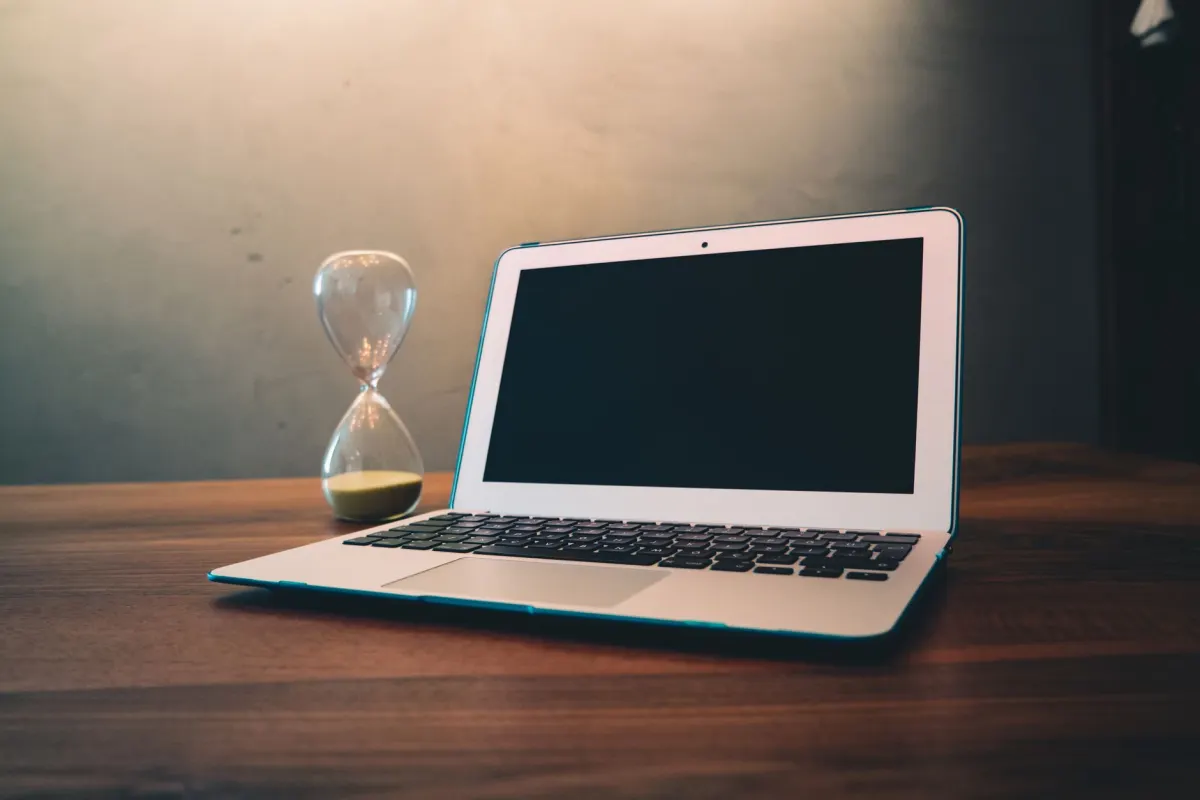 An hourglass on a desk beside a laptop, standing for the gap between a post going live and its first comment arriving.
