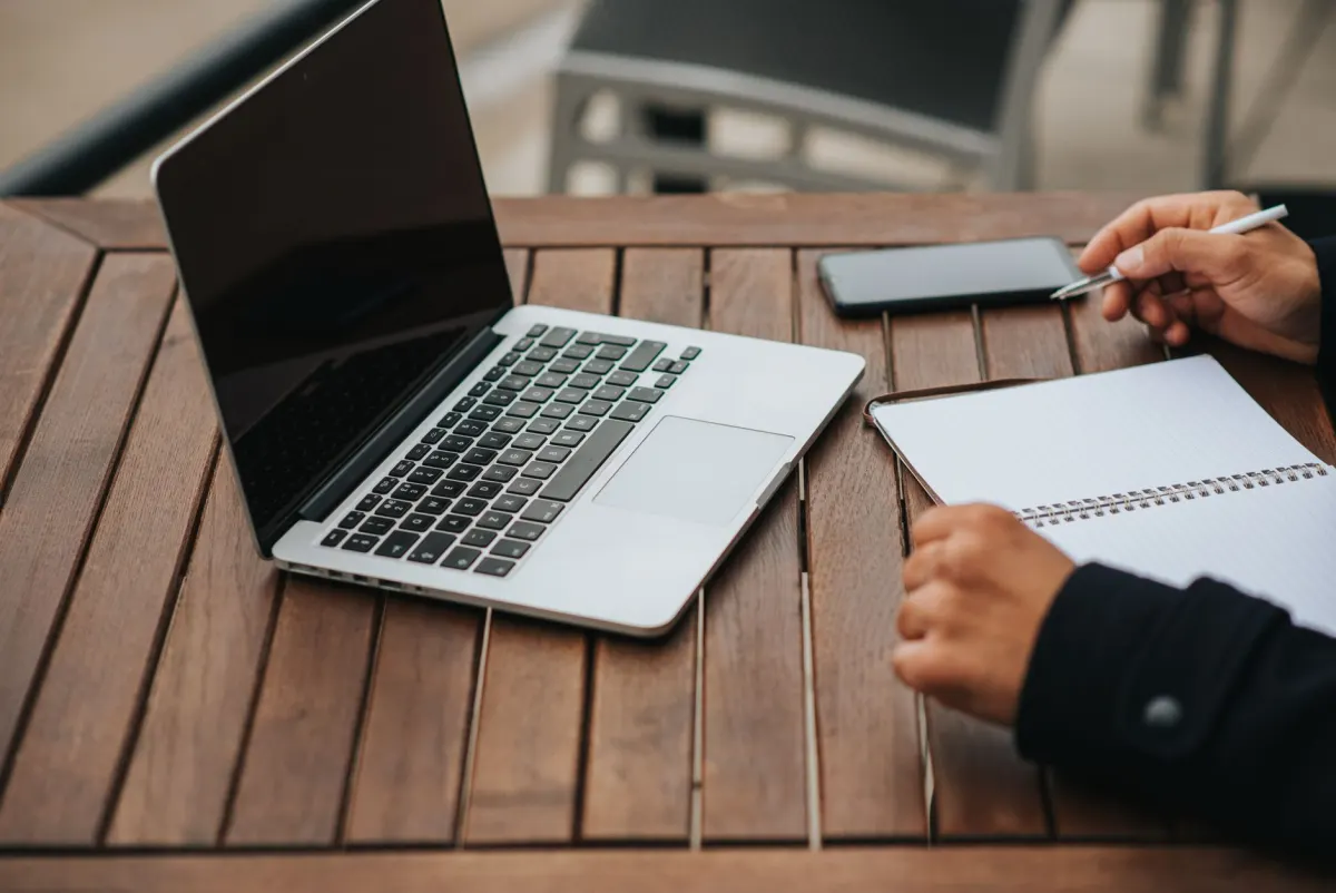 Une personne travaille sur un ordinateur portable avec un téléphone à côté, le quotidien de la gestion de plusieurs comptes sociaux.
