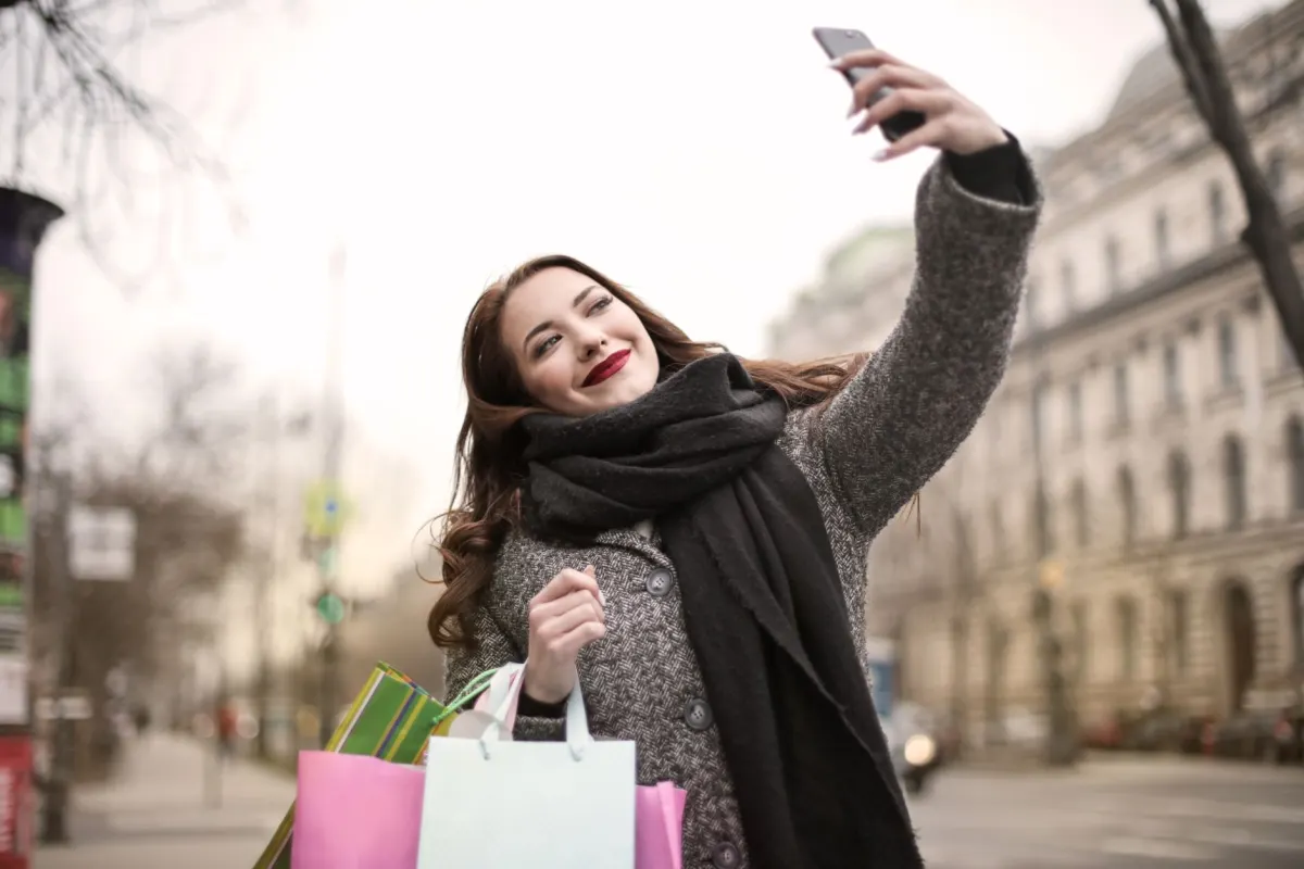 Ein Käufer schaut auf sein Handy und trägt Einkaufstüten, ein Sinnbild für den wiederkehrenden Kunden, den Retargeting-Kampagnen zurückholen sollen.