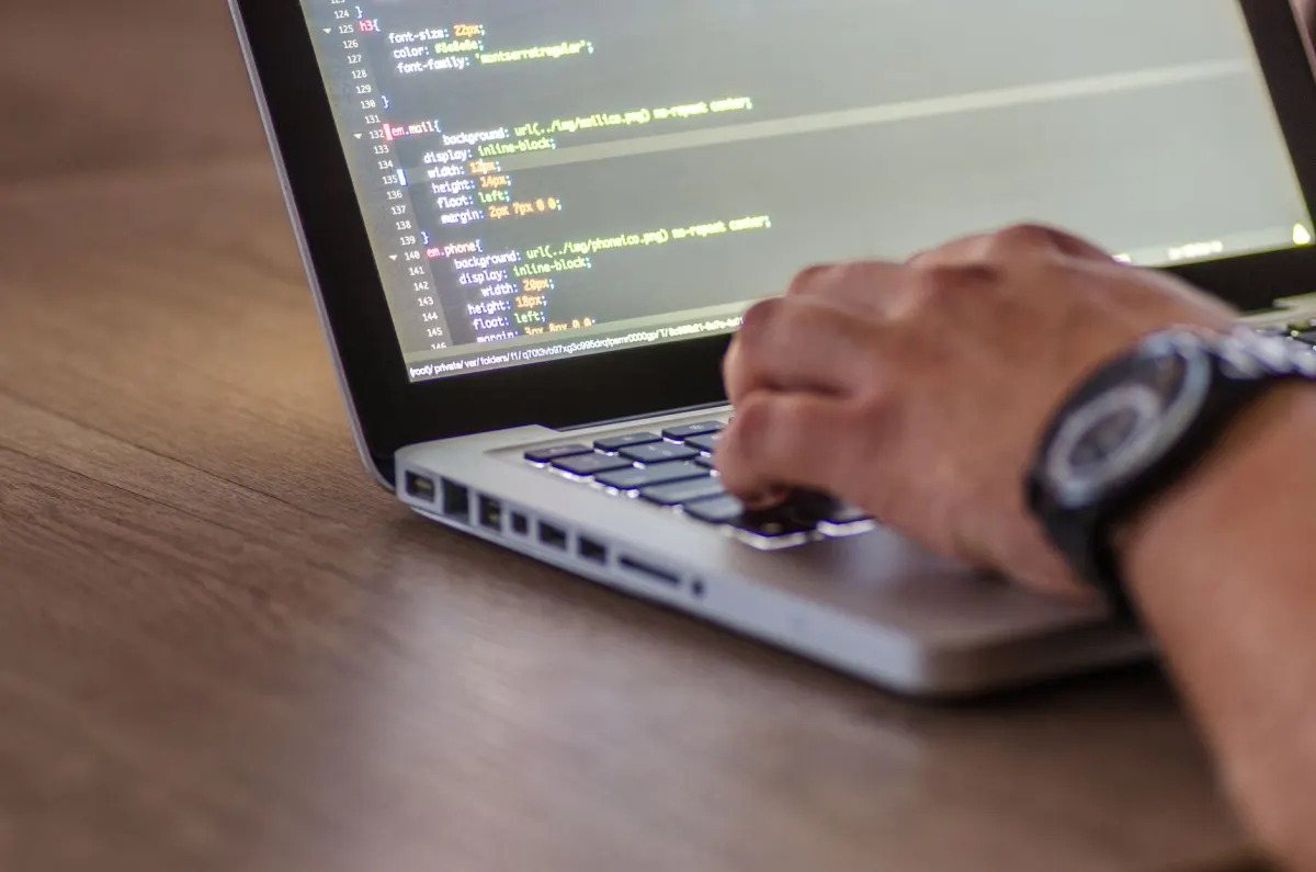 Un desarrollador escribe codigo en un portatil, junto a la seccion sobre herramientas de busqueda con IA para desarrolladores.