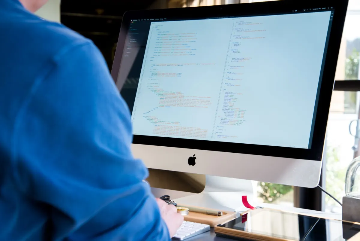 A programmer types code on a dual-monitor setup, illustrating the coding work these AI models compete on.