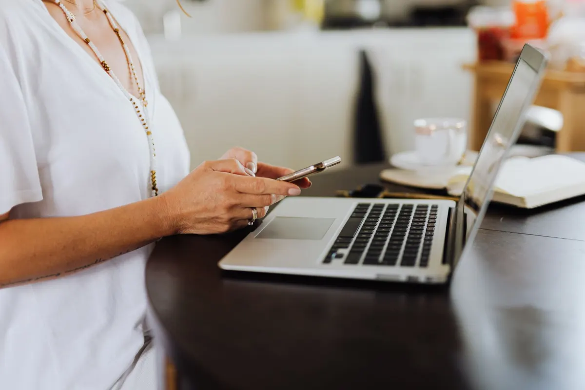 Un agent immobilier consulte une appli de messagerie sur son téléphone à côté d'un ordinateur portable, l'installation que couvre ce guide.